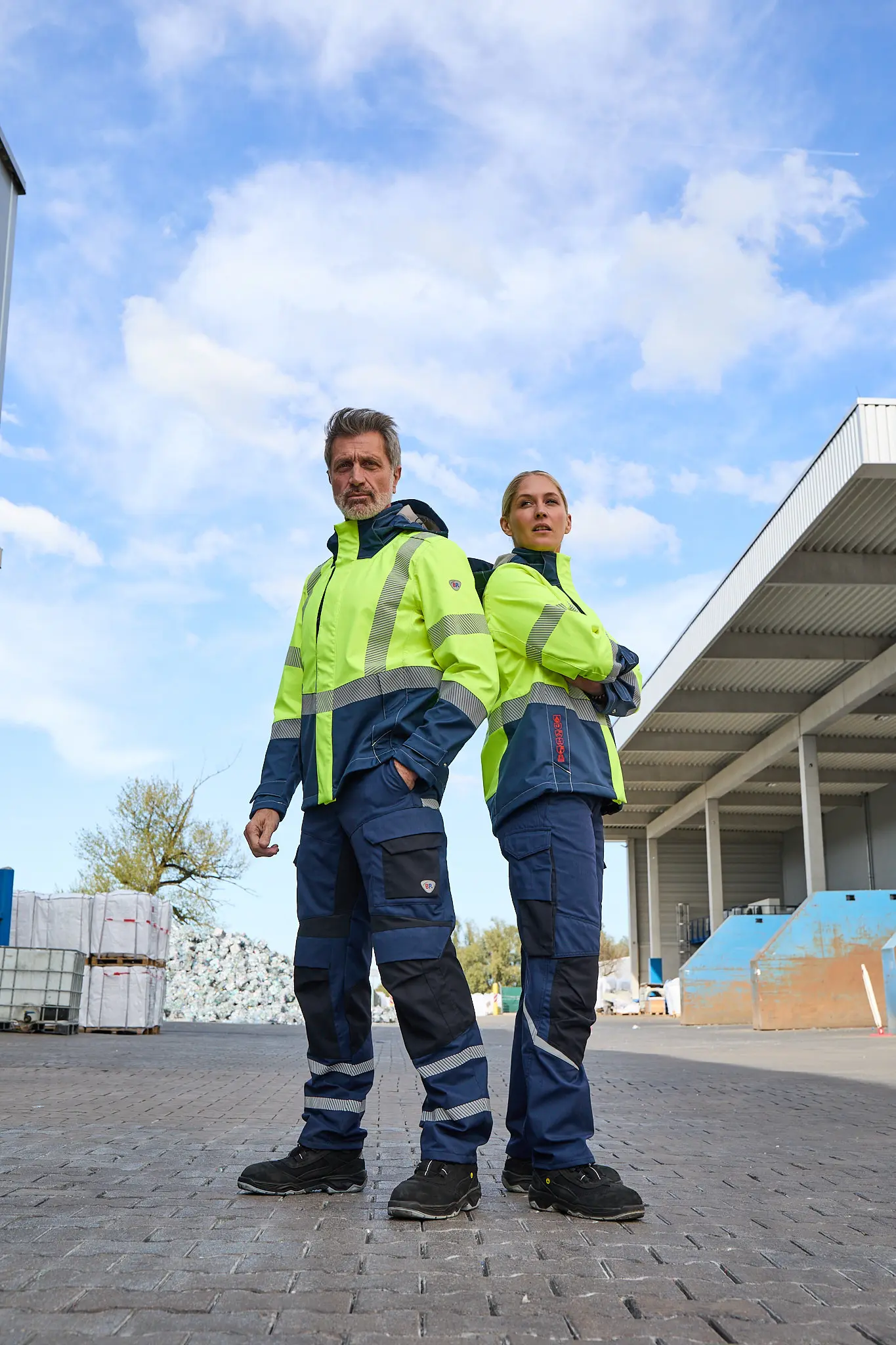 Zwei Models in BP-Warnschutzjacken stehen Rücken an Rücken vor Reiling-Gebäuden