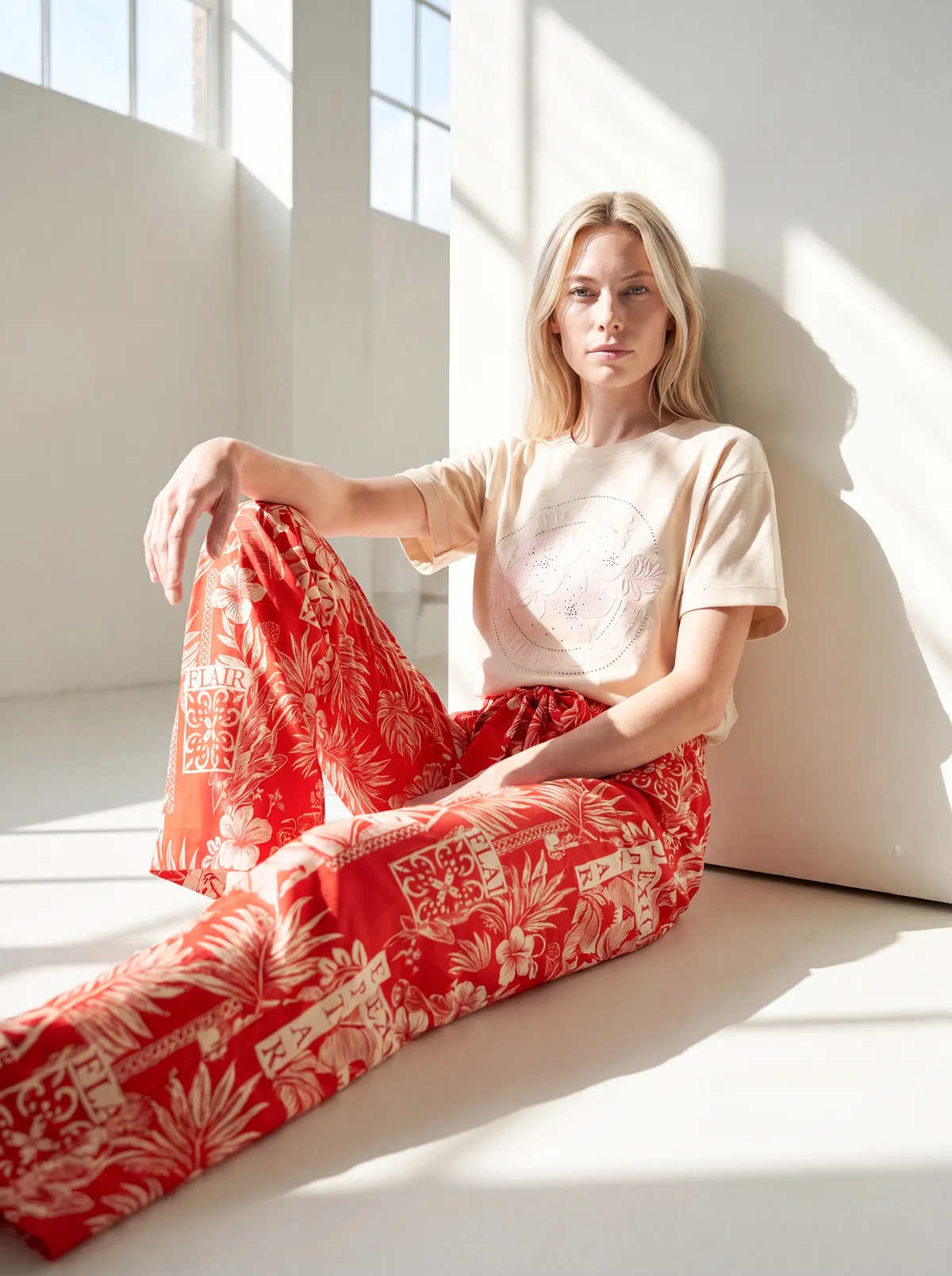 KI-Model trägt die rote Exotic-Print-Hose und das cremefarbene Shirt, sitzend