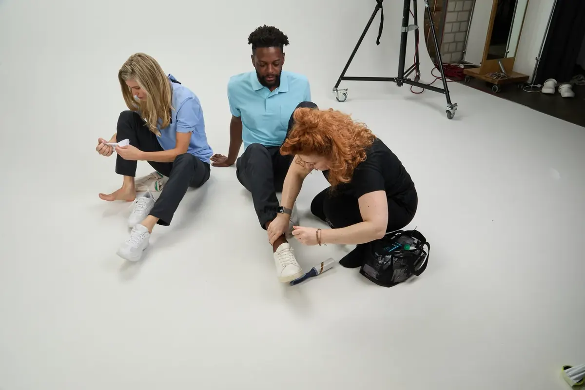 Making-of beim BP-Shooting: Stylistin richtet die Kleidung von zwei Models, die in Polos auf dem Studioboden sitzen