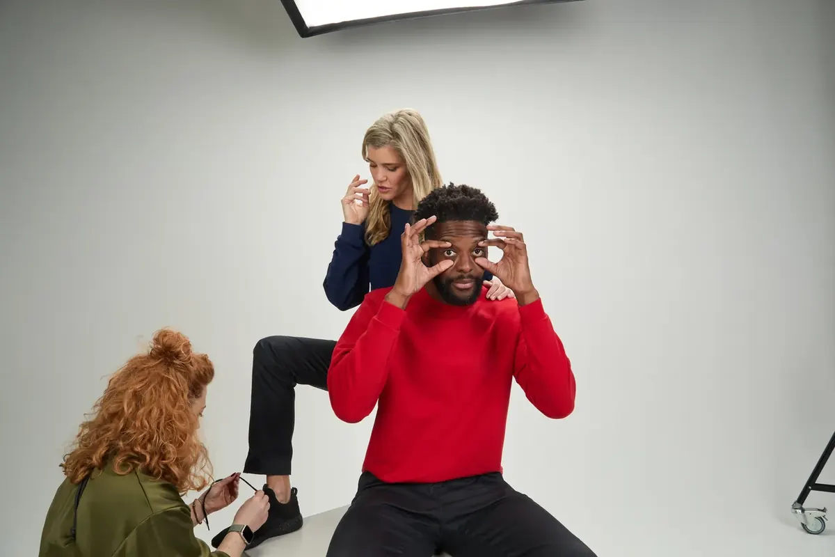 Making-of: Model im roten Sweatshirt macht Faxen, während die Stylistin die Schuhe richtet