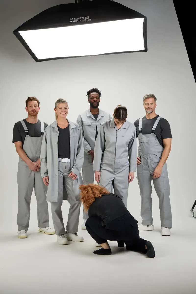 Making-of am ersten Shootingtag: fünf Models in grauer BP-Arbeitskleidung, die Stylistin richtet eine Hose