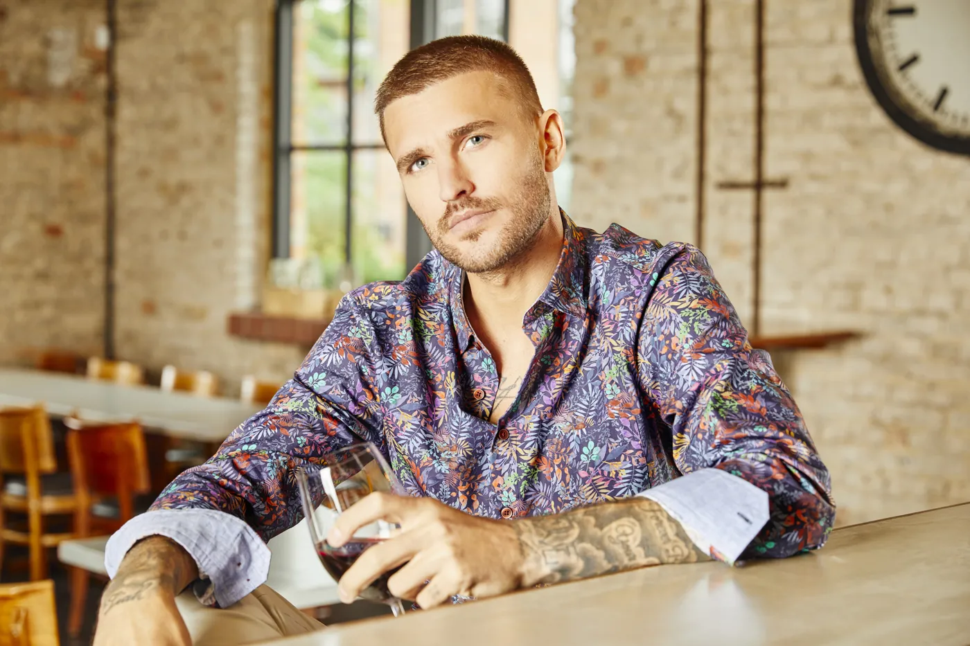Model im gemusterten Hemd mit Rotweinglas an einer Bar, Fashion-Shooting für HAUPT
